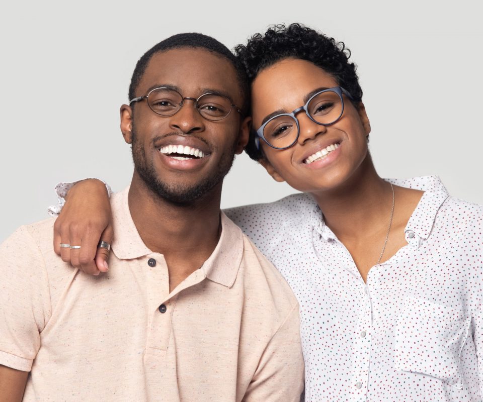 Head shot portrait African attractive married couple in glasses embracing smiling looking at camera posing isolated on grey background, love and relations, clients of photo shooting in studio concept